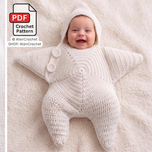 Puede incluir: Un saco de dormir de ganchillo blanco en forma de estrella con capucha, que presenta dos botones circulares en el lado superior izquierdo. El artículo se presenta como un patrón de ganchillo en PDF de AtenCrochet. El diseño tiene cinco puntas.