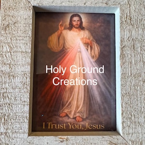 May include: Framed religious artwork featuring an image of Jesus with rays of red and white light emanating from his chest. The text "Holy Ground Creations" and "I Trust You, Jesus" are visible. The frame is a light, textured color.