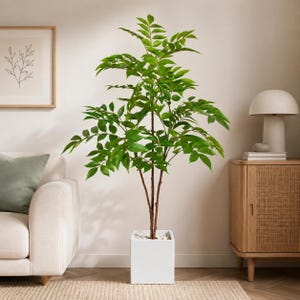 May include: A tall artificial plant with vibrant green leaves and thin brown stems, potted in a clean white square container filled with small white stones. The plant features multiple branches extending outward, creating a full, leafy appearance.