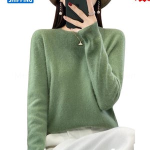 May include: A sage green crew neck sweater with long sleeves. The sweater has a soft, textured appearance. The image also includes a "Best Seller" sticker and a "Free Shipping" banner.