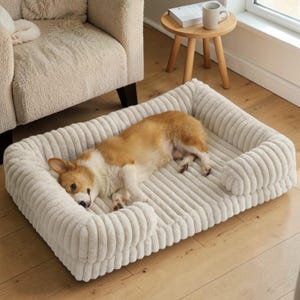 May include: A cream-colored, corduroy dog bed with a rectangular shape and raised sides. A brown and white corgi dog is lying inside the bed. The bed is on a wooden floor.