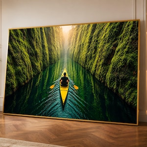 Puede incluir: Una gran pieza de arte mural rectangular en un marco dorado fino que presenta una fotografía de paisaje de una persona remando en un kayak amarillo brillante a través de un cañón fluvial estrecho y profundo con paredes rocosas cubiertas de musgo.