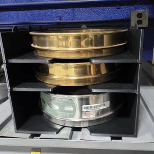 May include: A black plastic storage unit holding three sieves. The top two sieves are brass, and the bottom sieve is stainless steel. The bottom sieve has a label that reads "Testing Sieve" and "For Reference Only."