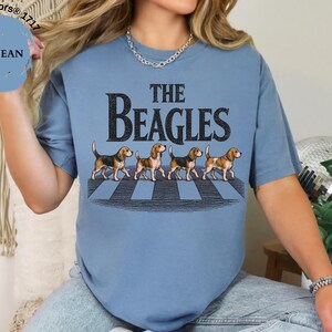 May include: Blue jean coloured t-shirt with the text "THE BEAGLES" in black, featuring an illustration of four beagles crossing a crosswalk. The shirt is a Comfort Colors 1717 style.