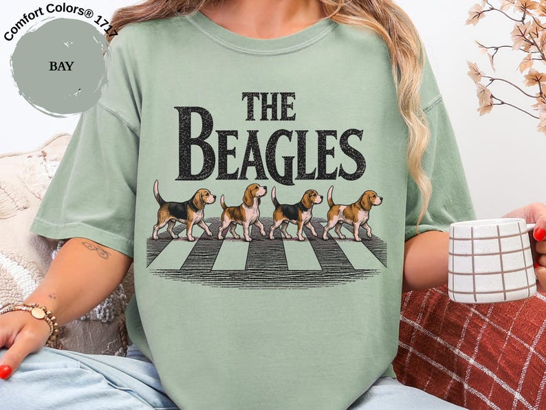 May include: A pale green t-shirt featuring the words "THE BEAGLES" and an image of four beagles crossing a zebra crossing. The shirt is a Comfort Colors 1717 style.