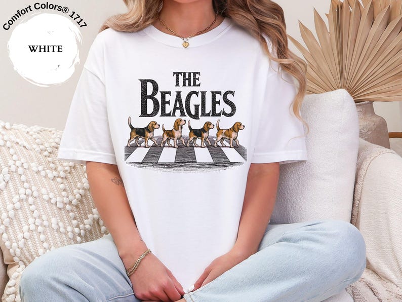 May include: White t-shirt with the words "THE BEAGLES" in a black font above an illustration of four beagles on a crosswalk. The shirt is a Comfort Colors 1717 style.