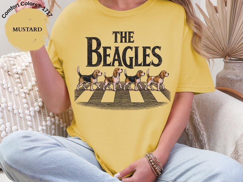May include: Mustard yellow t-shirt featuring the text "THE BEAGLES" above an illustration of four beagles on a zebra crossing. The shirt is a Comfort Colors 1717 style.