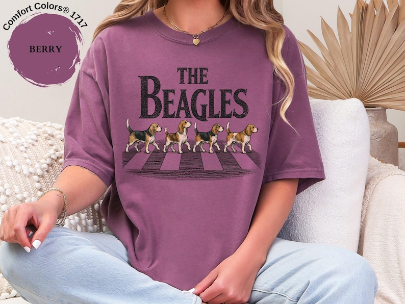 May include: Berry-coloured t-shirt with the words "The Beagles" and an image of four beagles on a zebra crossing. The shirt is a Comfort Colors brand.
