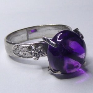 Puede incluir: Un anillo de plata con una gran amatista redonda de color p&uacute;rpura. El anillo tiene un dise&ntilde;o detallado en la banda.