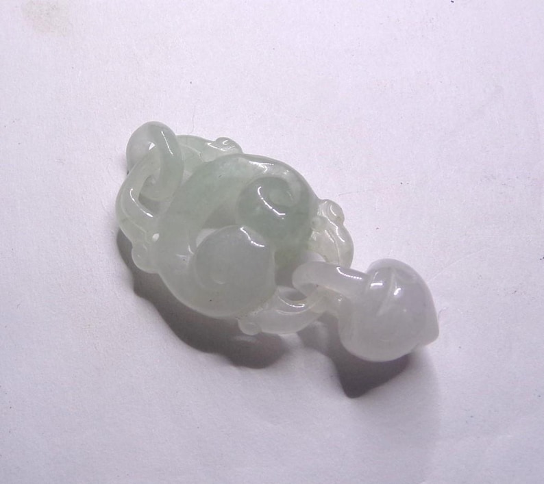 Peut inclure: Un pendentif en jade blanc sculpt&eacute; en forme de n&oelig;ud stylis&eacute; avec un d&eacute;tail en forme de c&oelig;ur. Le pendentif est lisse et poli.
