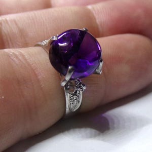 Puede incluir: Un anillo de plata con una gran amatista redonda de color p&uacute;rpura. El anillo tiene un delicado dise&ntilde;o floral.