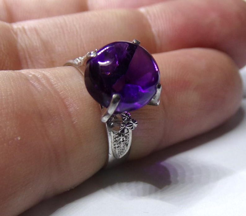 Puede incluir: Un anillo de plata con una gran amatista redonda de color p&uacute;rpura. El anillo tiene un delicado dise&ntilde;o floral.