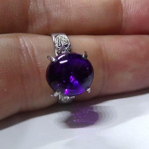 Puede incluir: Un anillo de plata con una gran amatista redonda y p&uacute;rpura engastada en garras.