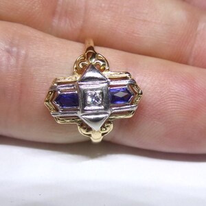 May include: A gold and silver ring with a geometric design. The ring features two blue sapphires and a single diamond in the center.