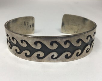 May include: A silver bracelet with a black wave design. The bracelet is stamped with the number "125".