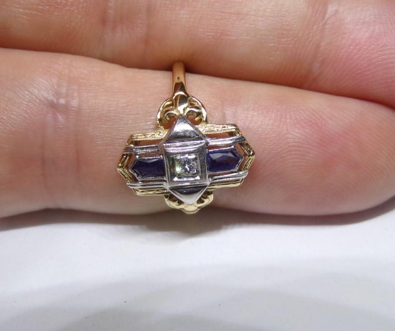 May include: A gold ring with a geometric design featuring a central diamond and two blue sapphires.