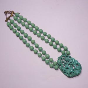 May include: A double strand necklace made of light green beads with a carved green pendant featuring a stylized figure.