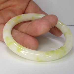 May include: A white jade bangle with green swirls. The bangle is smooth and polished.