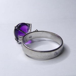 Puede incluir: Un anillo de plata con una gran amatista redonda y p&uacute;rpura engastada en un dise&ntilde;o de jaula.