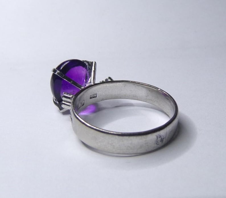 Puede incluir: Un anillo de plata con una gran amatista redonda y p&uacute;rpura engastada en un dise&ntilde;o de jaula.