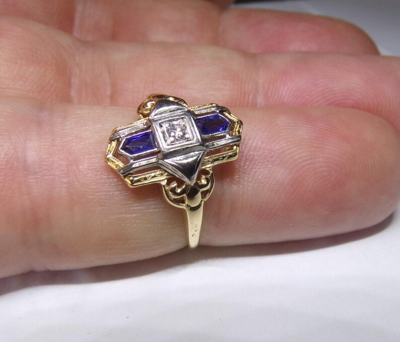 May include: A gold and silver ring with a geometric design featuring a central diamond and two blue sapphires.