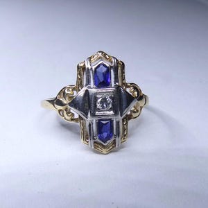 May include: A gold and silver ring with a geometric design featuring three blue sapphires and a single diamond.