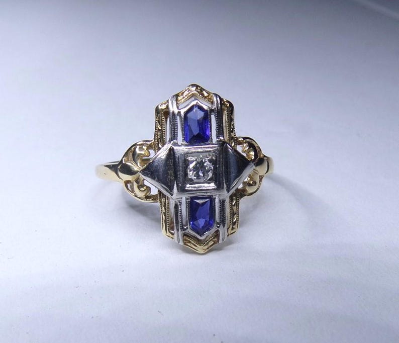 May include: A gold and silver ring with a geometric design featuring three blue sapphires and a single diamond.