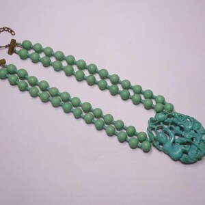 May include: A double strand necklace with a carved jade pendant. The necklace is made of light green beads and has a gold clasp.