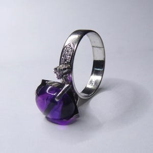 Puede incluir: Un anillo de plata con una gran amatista redonda y p&uacute;rpura. El anillo tiene una banda simple y un peque&ntilde;o acento de diamante.