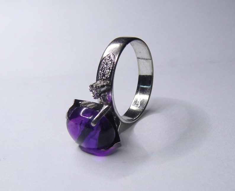 Puede incluir: Un anillo de plata con una gran amatista redonda y p&uacute;rpura. El anillo tiene una banda simple y un peque&ntilde;o acento de diamante.