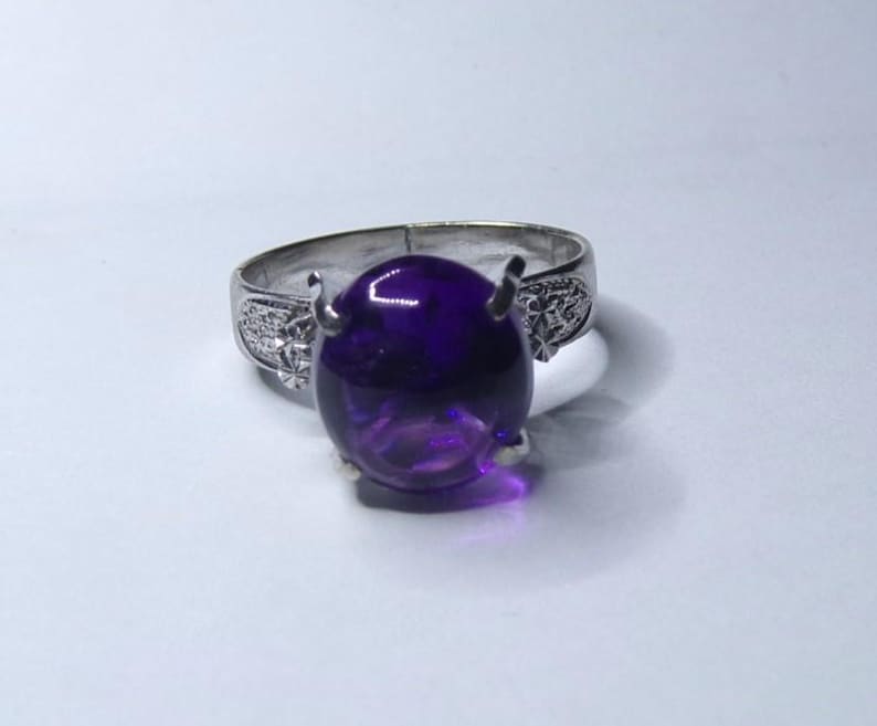 Puede incluir: Un anillo de plata con una gran amatista ovalada. El anillo tiene un dise&ntilde;o floral en la banda.