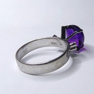 Puede incluir: Un anillo de plata con una gran amatista ovalada. El anillo est&aacute; engastado con piedras preciosas m&aacute;s peque&ntilde;as en la banda y tiene un sello en el interior de la banda.