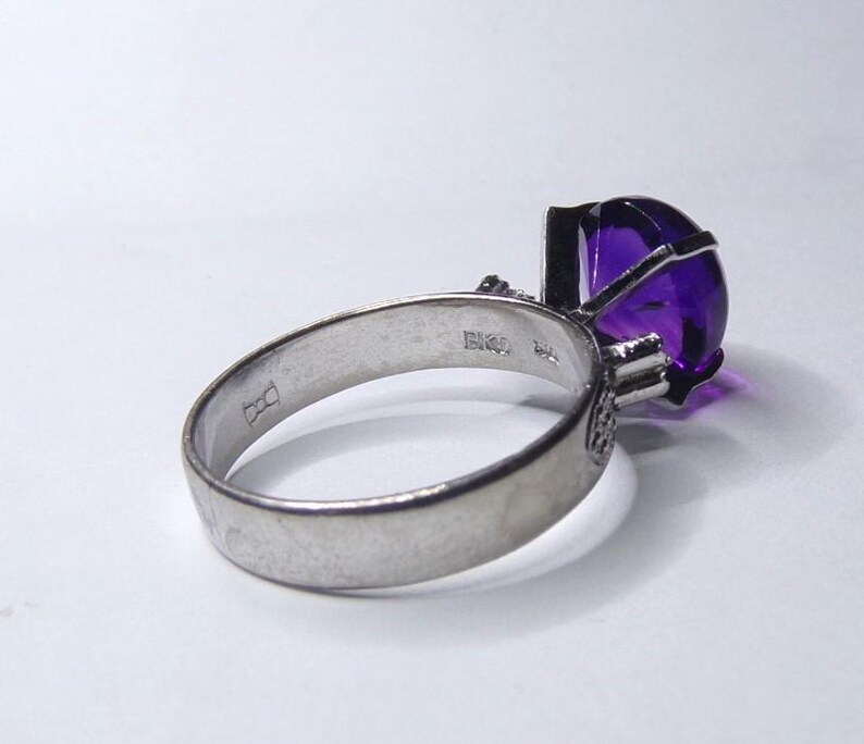 Puede incluir: Un anillo de plata con una gran amatista ovalada. El anillo est&aacute; engastado con piedras preciosas m&aacute;s peque&ntilde;as en la banda y tiene un sello en el interior de la banda.