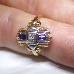 May include: A gold ring with a white diamond and two blue sapphires set in a geometric design.