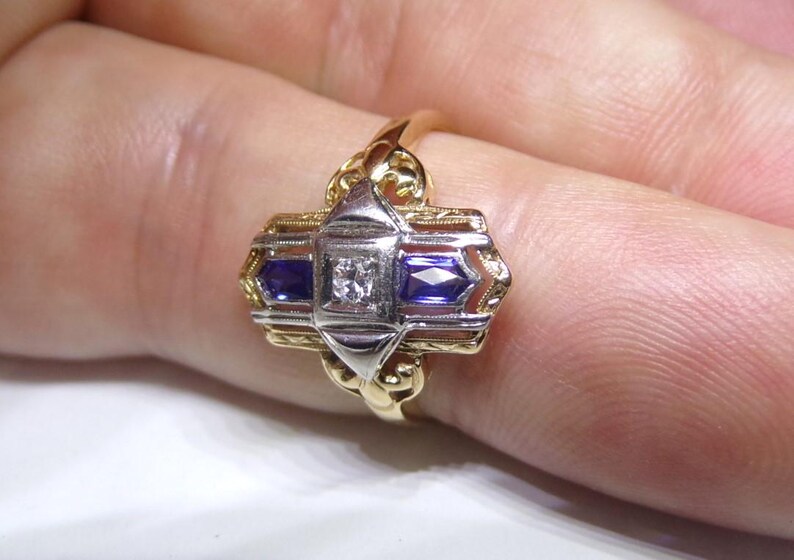 May include: A gold ring with a white diamond and two blue sapphires set in a geometric design.