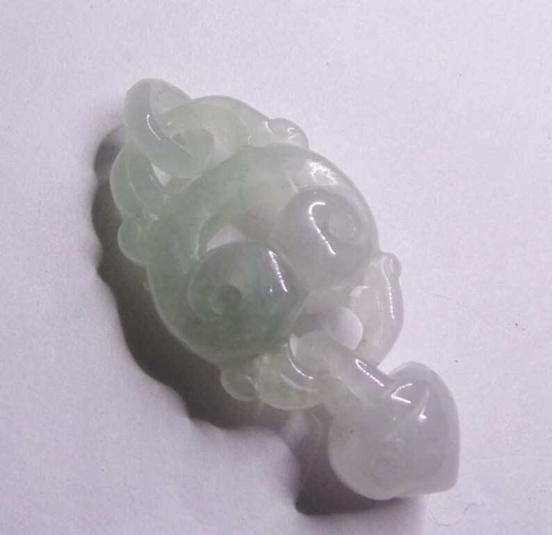 Peut inclure: Un pendentif en jade blanc avec des sculptures complexes en forme de n&oelig;ud. Le pendentif est lisse et poli, avec une qualit&eacute; d&eacute;licate et translucide.