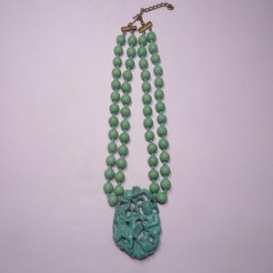 May include: A double strand necklace made of green beads with a carved green jade pendant featuring a figure of a person.