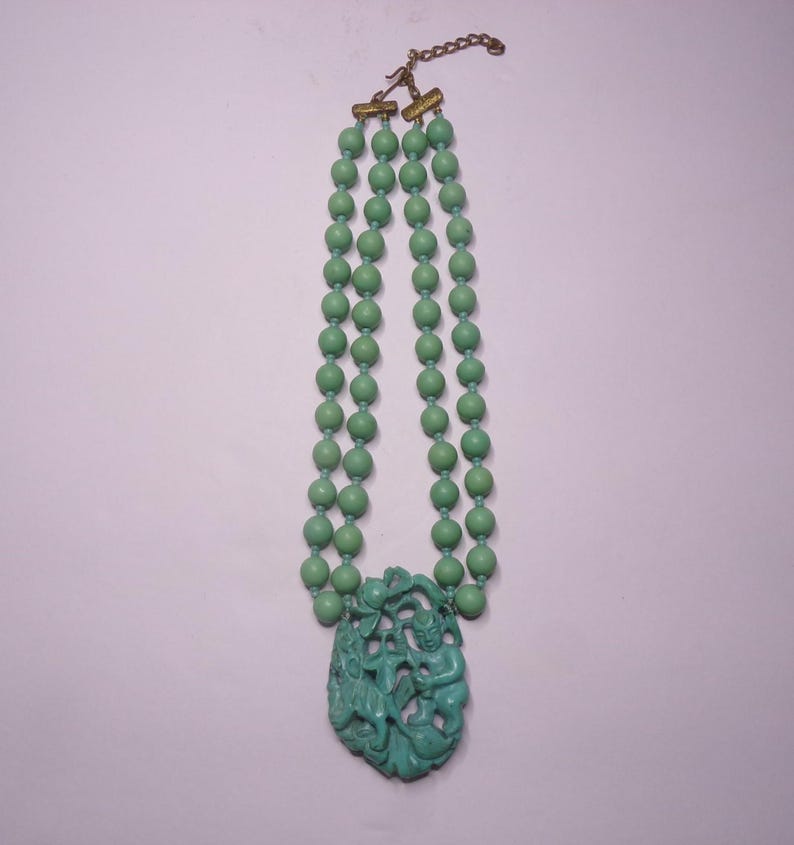 May include: A double strand necklace made of green beads with a carved green jade pendant featuring a figure of a person.