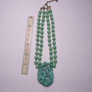 May include: A double strand necklace with green beads and a carved green pendant featuring a mythical creature. The necklace is 18 inches long.