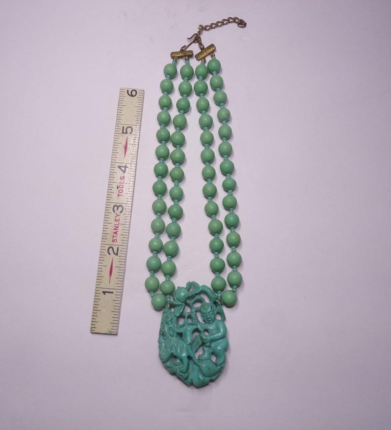 May include: A double strand necklace with green beads and a carved green pendant featuring a mythical creature. The necklace is 18 inches long.