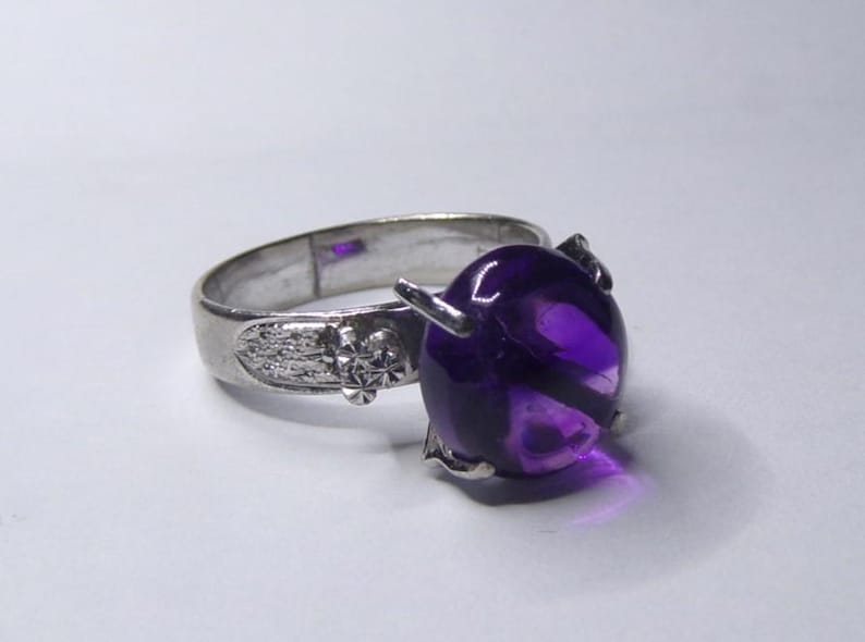 Puede incluir: Un anillo de plata con una gran amatista redonda de color p&uacute;rpura. El anillo tiene un dise&ntilde;o detallado en la banda.