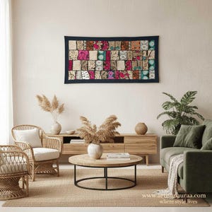 May include: A living room with a patchwork wall hanging with a dark blue border. The room includes wicker chairs, a wooden coffee table, a green sofa, and decorative plants. The website address www.artisanauraa.com is visible.