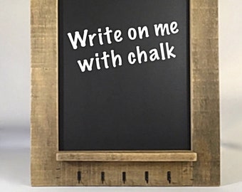 May include: A rectangular chalkboard with a rustic wooden frame. The black chalkboard surface has the text "Write on me with chalk" in white. The frame has a small shelf at the bottom with four small hooks.