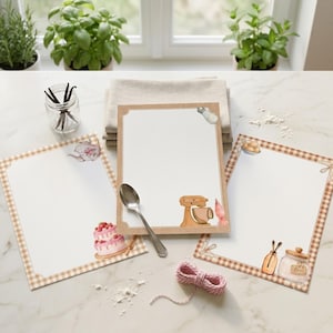 May include: Three rectangular sheets of stationery with a tan gingham border. The sheets feature watercolor illustrations of baking items including a tiered cake, a stand mixer, a piping bag, a jar of flour, and a teapot. A silver spoon rests on top.