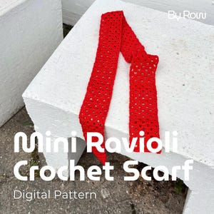 Könnte beinhalten: Ein leuchtend roter, offen gewebter Häkelschal, der mit "Mini Ravioli Crochet Scarf" und "Digital Pattern" beschriftet ist. Der Schal ist über eine weiße Oberfläche drapiert. In der oberen rechten Ecke steht "By Row."