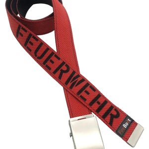 May include: A red fabric belt with a black metal buckle and a black tip. The word FEUERWEHR is printed in large black capital letters along the length of the strap. A small black tag with the white and red text FireBoot is attached near the tip.