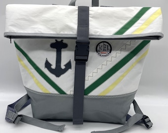 May include: White and gray backpack with green and yellow stripes, an anchor graphic, and a black buckle closure. The bag has adjustable gray straps and a top handle. The bag has the text "KEL" on it.