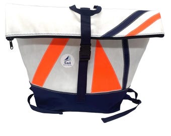 Può includere: Uno zaino roll-top bianco con dettagli blu navy e pannelli triangolari arancioni brillanti. La borsa presenta una cinghia centrale blu navy con fibbia in plastica, una base blu navy e una toppa circolare con il testo Sail Generation.