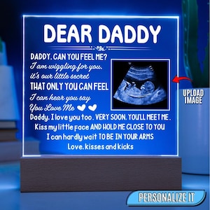May include: A blue LED light with the words "DEAR DADDY" and a message about a baby. The light includes an ultrasound image and sits on a wooden base. The text reads "Daddy, I love you too. Very soon, you'll meet me."