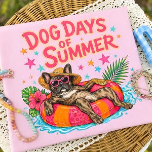 Op de afbeelding: Roze T-shirt met de tekst "Dog Days of Summer". Het ontwerp toont een Franse bulldog met zonnebril en strohoed, liggend op een opblaasbare ring. Kleurrijke sterren en tropische bloemen omringen de hond.